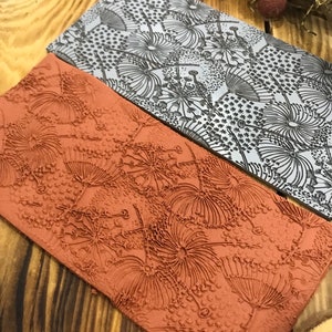 May include: Two rectangular rubber stamps with a raised design of stylised dandelion flowers. The top stamp is grey and the bottom stamp is orange.