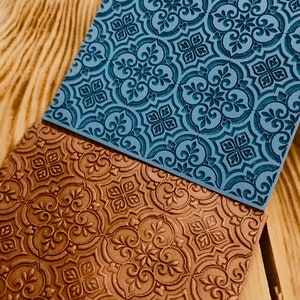 Pode incluir: Dois tapetes de silicone para cozedura com um padrão em relevo decorativo. O tapete superior é azul e o tapete inferior é castanho.
