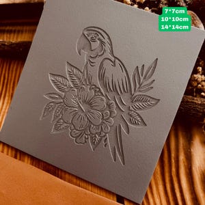 May include: A gray rubber stamp with a detailed design of a parrot perched on a flower. The stamp is available in three sizes: 7x7 cm, 10x10 cm, and 14x14 cm.