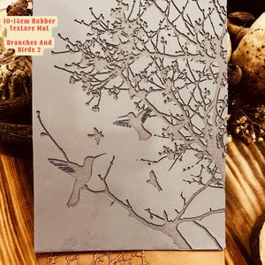 May include: A gray rubber texture mat with a design of branches and two hummingbirds. The text "10-14cm Rubber Texture Mat Branches And Birds 2" is printed on the mat.
