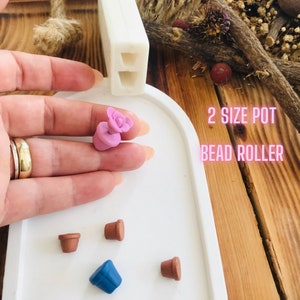 Op de afbeelding: Een set siliconen mallen voor het maken van kralen van polymer clay. De mallen zijn gevormd als bloempotten en zijn verkrijgbaar in twee maten. De tekst "2 size pot bead roller" is zichtbaar in de afbeelding.