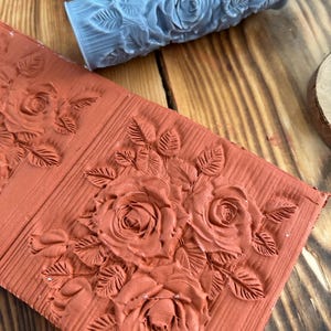 Peut inclure: Un tampon en argile rouge avec un motif en relief de roses et de feuilles. Le tampon est utilisé pour créer des motifs décoratifs sur les surfaces.