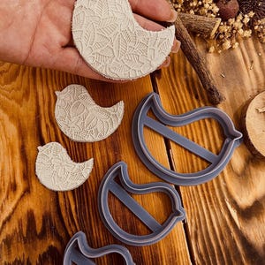 May include: Three different sized bird-shaped cookie cutters, two are made of white clay and one is made of gray plastic.