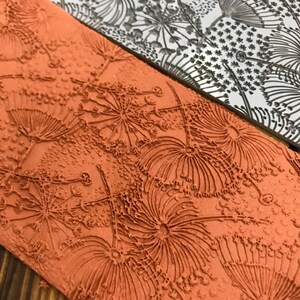 May include: A close-up of a textured, orange-brown rubber stamp with a design of stylised flowers. The stamp is made of a soft, flexible material and has a raised design.