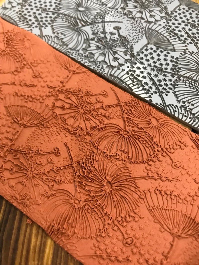 May include: A close-up of a textured, orange-brown rubber stamp with a design of stylised flowers. The stamp is made of a soft, flexible material and has a raised design.