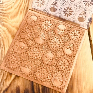 May include: A brown rubber stamp with a repeating pattern of skulls and snowflakes. The stamp is on a wooden surface.