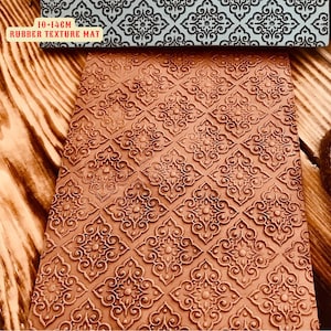 May include: A 10x14cm rubber texture mat with a repeating pattern of intricate, detailed, ornate designs. The mat is brown and the design is raised and textured.