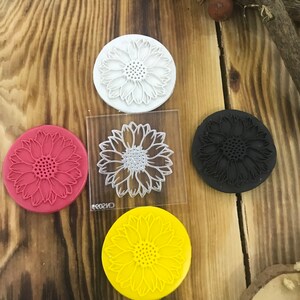 May include: Four round silicone stamps with a sunflower design. The stamps are white, red, black, and yellow.