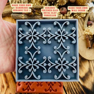 Puede incluir: Un molde de silicona azul con un diseño cuadrado que presenta un patrón repetitivo de motivos florales estilizados. El molde está etiquetado como "Make Your Own Handmade Ceramic Tile" y "Ceramic Polymer Clay Metal Clay Porcelain".