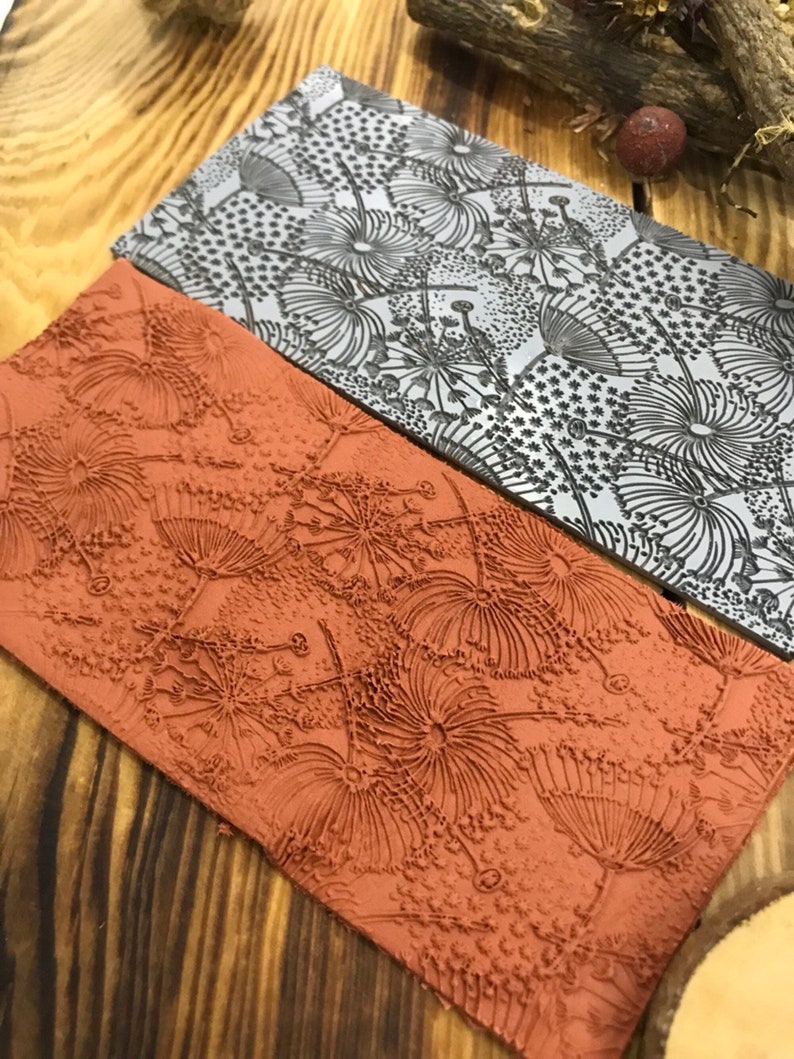 May include: Two rectangular rubber stamps with a raised design of stylised dandelion flowers. The top stamp is grey and the bottom stamp is orange.