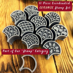 May include: Set of 11 ceramic stamps with different geometric and floral designs. The stamps are shaped like half-circles and are arranged in a semi-circle on a wooden surface. The text "11-Piece Coordinated CERAMIC Stamp Set" and "Part of Our "Stamp" Category" is visible in the image.