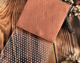 May include: A clear acrylic stamp sheet with a white polka dot pattern. The sheet is placed on top of a brown rubber stamp with a similar polka dot pattern.