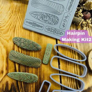 Può includere: Un set di quattro fermagli per capelli verdi e dorati con motivi di foglie e fiori. Il set include uno stampo in silicone con vari disegni per realizzare fermagli per capelli. Il testo "Hairpin Making Kit2" è visibile nell'immagine.