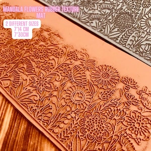 Può includere: Due tappetini in gomma con texture e un motivo floreale. I tappetini sono arancioni e grigi. Il testo "MANDALA FLOWERS RUBBER TEXTURE MAT" e "2 DIFFERENT SIZES 7"14 CM 7"30CM" è stampato sui tappetini.
