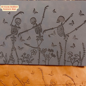 Puede incluir: Una estera de textura de goma gris con un diseño de tres esqueletos bailando en un campo de flores. La estera mide 10-14 cm y tiene una superficie texturizada.
