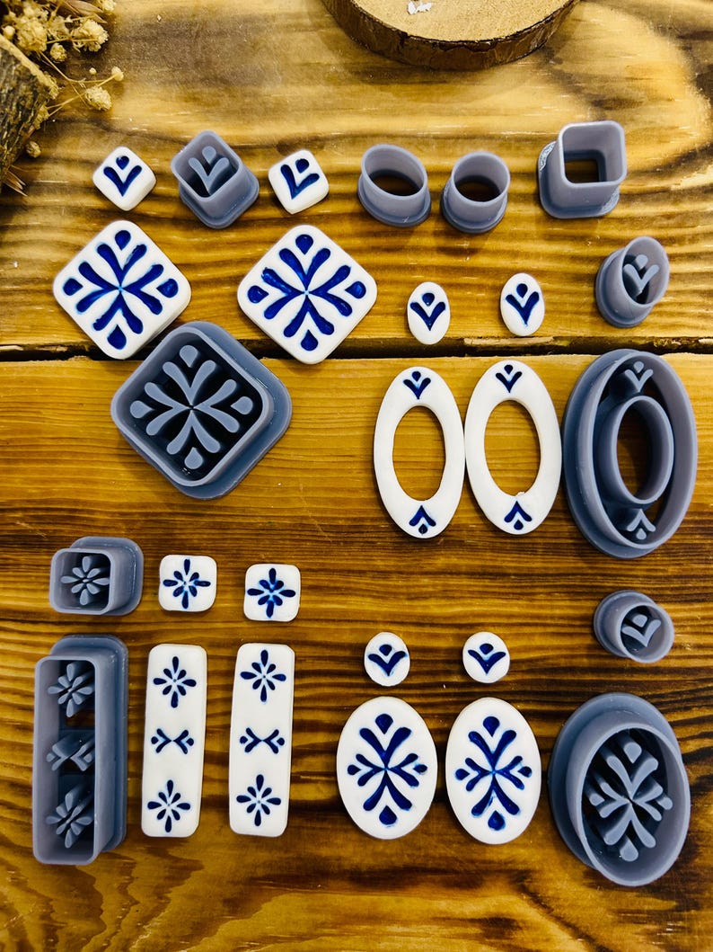 May include: A set of 19 polymer clay cutters featuring various geometric shapes and designs, including squares, ovals, and circles. The cutters are in shades of gray and white, with some featuring blue and white patterns.