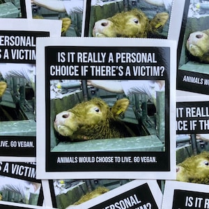 May include: Square sticker with a black border and text that reads "IS IT REALLY A PERSONAL CHOICE IF THERE'S A VICTIM?" and "ANIMALS WOULD CHOOSE TO LIVE. GO VEGAN." The image shows a cow in a metal enclosure.