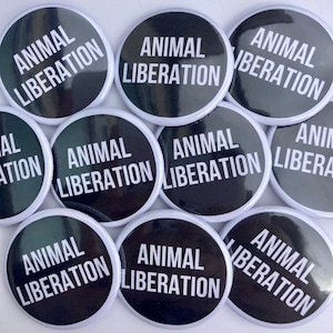 May include: A collection of black and white round buttons with the text "ANIMAL LIBERATION" printed in white on a black background.