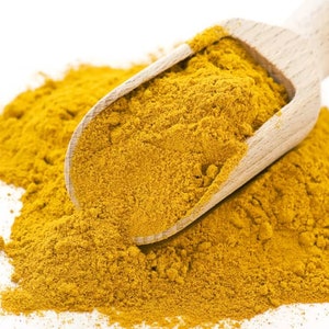 May include: A wooden scoop filled with bright yellow turmeric powder, spilling onto a white surface.