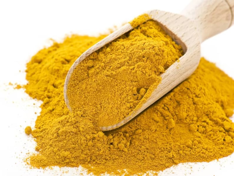 May include: A wooden scoop filled with bright yellow turmeric powder, spilling onto a white surface.