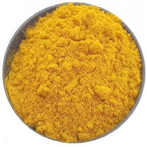 May include: A close-up view of a bowl filled with bright yellow turmeric powder.