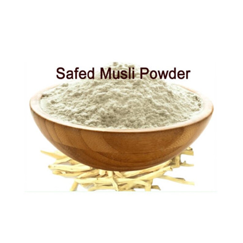 May include: A wooden bowl filled with a light beige powder labelled "Safed Musli Powder". The powder is surrounded by dried, light brown roots.