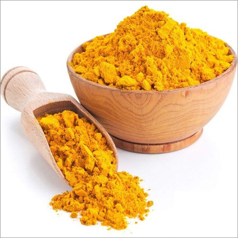 May include: A wooden scoop filled with bright yellow turmeric powder, spilling out onto a white surface. The powder is also in a wooden bowl.