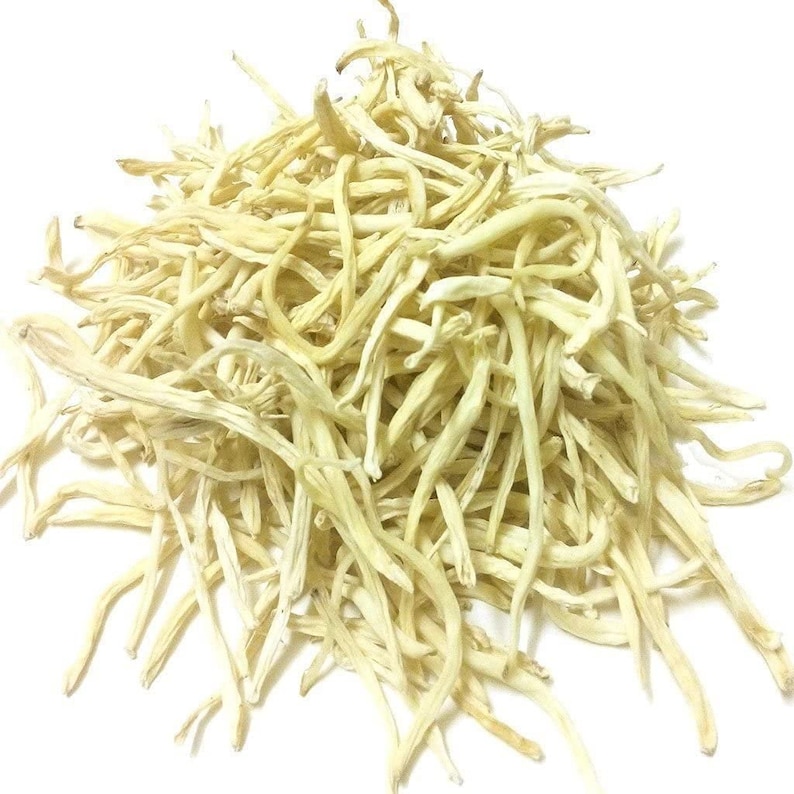 May include: A pile of dried, pale yellow lily buds against a white background. The buds are long, thin, and slightly curved, with a textured appearance. The image is a close-up, highlighting the details of the dried flowers.