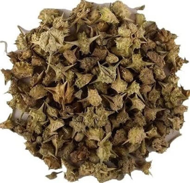 May include: A close-up image of a pile of dried, spiky, star-shaped plant parts. The color palette is dominated by shades of brown and tan, with some hints of green. The texture appears rough and dry, suggesting a natural product.