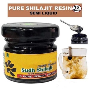 May include: A small glass jar with a black lid containing a dark brown semi-liquid substance. The jar has a yellow label with the text "100% Natural Sudh Shilajit Health Supplement A PURE HERBAL PRODUCT". The jar is sitting on a white surface. A spoon is scooping the substance out of the jar and a glass of water with the substance dissolved in it is in the background.