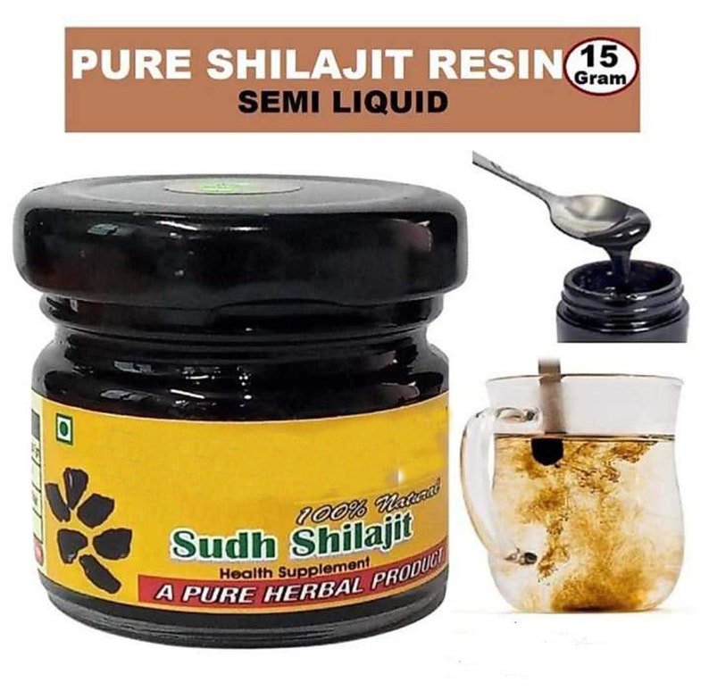 May include: A small glass jar with a black lid containing a dark brown semi-liquid substance. The jar has a yellow label with the text "100% Natural Sudh Shilajit Health Supplement A PURE HERBAL PRODUCT". The jar is sitting on a white surface. A spoon is scooping the substance out of the jar and a glass of water with the substance dissolved in it is in the background.