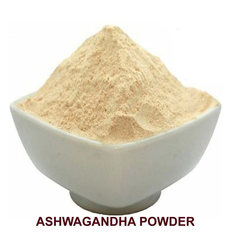 May include: A white bowl filled with light brown Ashwagandha powder. The bowl is sitting on a white surface. The text "ASHWAGANDHA POWDER" is printed in dark brown letters below the bowl.