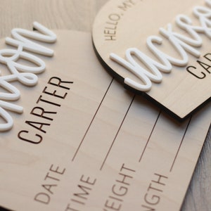 May include: Two circular wooden birth announcement signs featuring the name Jackson Carter in raised white script lettering. The signs include engraved text that reads Hello, My Name Is, Date, Time, Weight, and Length with lines for writing.