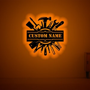 May include: Black metal wall art featuring a circle of tools with a banner that says "CUSTOM NAME".