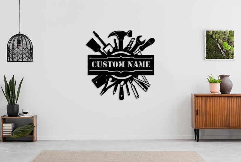 May include: Black metal wall art featuring a circle of tools, including a hammer, wrench, screwdriver, and saw. The circle is surrounded by a banner with the text "CUSTOM NAME".