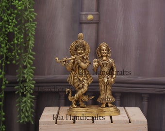 May include: Gold-toned metal statue of Radha Krishna, a Hindu deity couple, standing on a wooden base. The statue is intricately detailed and features the couple playing a flute and holding a flower.