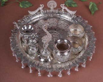 May include: A silver tray with a peacock design and a set of silver bowls and containers. The tray has a beaded fringe around the edge.