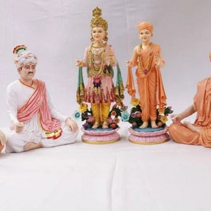 May include: Five colorful figurines of people sitting in a meditative pose. The figurines are made of painted resin and are arranged in a semi-circle on a white surface.