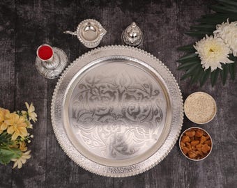 Puede incluir: Una bandeja de plata con un diseño adornado, rodeada de cuencos y recipientes de plata, algunos de los cuales contienen polvo rojo, arroz blanco y trozos marrones. La bandeja está sobre una superficie gris oscuro.