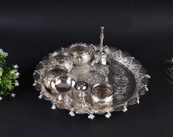 Può includere: Vassoio da portata argentato ornato con più scomparti e dettagli decorativi. Il vassoio include piccole ciotole, un contenitore centrale e un pezzo alto e sottile. Il design presenta motivi intricati e un bordo smerlato.