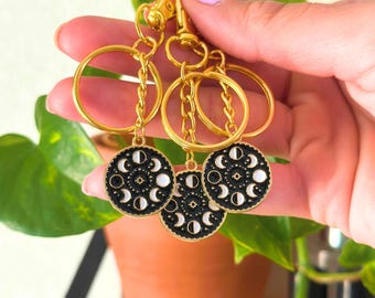 May include: Gold key chain with three black and white moon phase charms. The charms are round and have a gold rim.