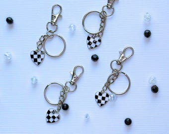 May include: Four silver keychains with black and white checkered heart charms. The keychains are on a white background.