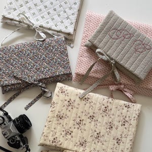 Pode incluir: Uma variedade de bolsas de tecido acolchoado com vários padrões florais e cores. As bolsas são em branco, rosa e estampados florais, com fechos de laço. Uma câmara vintage também é visível.