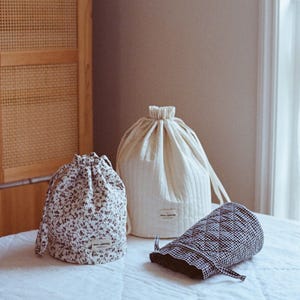 Könnte beinhalten: Drei gesteppte Beutel mit Kordelzug in verschiedenen Mustern. Ein Beutel ist weiß, einer ist floral und einer ist schwarz-weiß kariert.