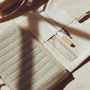 K&ouml;nnte beinhalten: Cremefarbene Federtasche aus Canvas mit floral gemusterter Stepph&uuml;lle. Ein Lineal, Stift und Bleistift sind sichtbar. Die Tasche ist ge&ouml;ffnet und zeigt ihren Inhalt. Das Design ist weich und vintage.