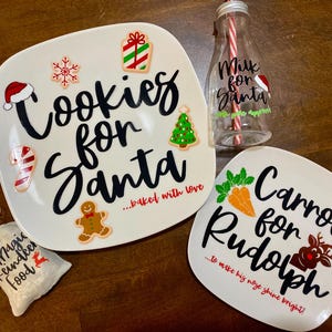 May include: A white square plate with black text reading Cookies for Santa, a white plate with black text reading Carrots for Rudolph, a clear glass bottle with a red and white straw, and a small white fabric bag labeled Magic Reindeer Food.