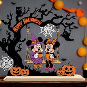 May include: A Halloween-themed wooden decoration featuring Mickey and Minnie Mouse on a swing under a tree. The tree has the words "HAPPY HALLOWEEN" and is decorated with pumpkins, bats, and spiderwebs. Mickey wears a witch hat and Minnie has a bow.