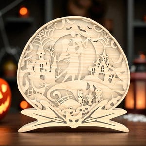 Puede incluir: Decoración de Halloween de madera con un diseño en capas que representa una casa embrujada, murciélagos y personajes. La decoración está sostenida por una base en forma de murciélago.