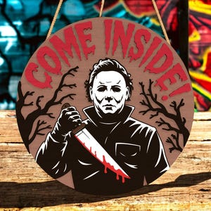 May include: Round wooden sign with the text "COME INSIDE!" in red, featuring a black and white illustration of a masked figure holding a bloody knife. The sign has a brown background with tree silhouettes and is suspended by a rope.