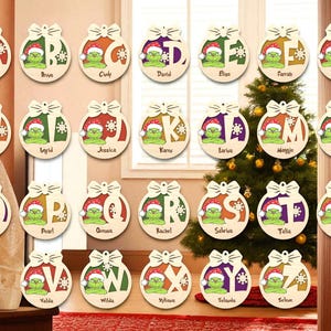 May include: Wooden Christmas ornaments featuring a Grinch character wearing a Santa hat, with letters and names. The ornaments are round with a bow at the top and snowflake accents. The names include Ava, Bruye, Cindy, David, Elise, Farrah, Gyve, Hawa, Ingrid, Jessica, Karev, Lariva, Maggie, Madia, Olivia, Pearl, Quena, Rachel, Sabriva, Talia, Udele, Valda, Wilda, Xylaya, Yolanda, and Zeleve.